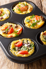 Tasty hot egg muffins with bacon, tomatoes, spinach and mushrooms close-up in a baking dish. vertical