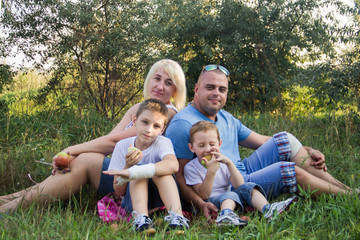 Happy parents of two boys relax in nature and eat apples