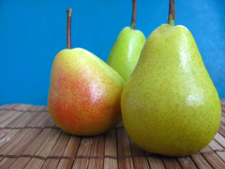 Three juicy ripe pears lie on a wooden table, behind a blue background. Autumn harvest of fruits....