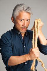 Hombre de mediana edad de origen japonés con una cuerda en sus manos y mirada amenazadora y muy...
