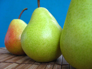 Group of mellow ripe green pears. Three piece of pears stand tails up on a wooden table. Autumn harvest of fruits. Crop view.