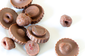 Homemade raw chocolate sweet candies with raspberries inside on white plate. Top view. Delicious candies seem to fly in the air.