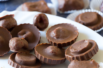 Homemade raw chocolate sweet candies with raspberries inside with droplets of water and raspberry juice on surface on white plate.