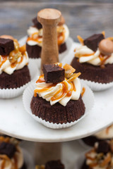 Chocolate cupcakes with cream cheese frosting, salted caramel sauce, brownie bites and toffees. Marble cakestand on grey wooden background.