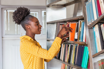 Young black woman looking for a book in library. people, knowledge, education and school concept -...