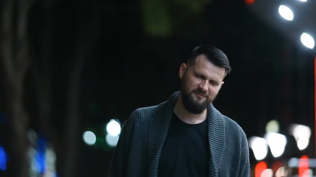 Close-up of a handsome bearded man nodding his head in agreement, then raising his hand in farewell, leaving the evening street and dancing happily. Glad to say goodbye