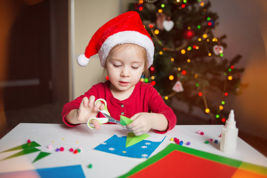 a little girl makes a card application of colored paper on the background of the Christmas tree. the concept of new year kids creativity