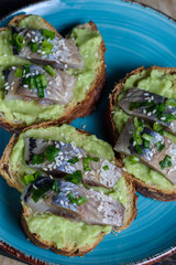 Avocado and herring sandwiches sprinkled with spring onions on grain bread top view on a plate close up