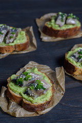 Avocado and herring sandwiches sprinkled with spring onions on grain bread top view on a paper napkin on a dark wooden background