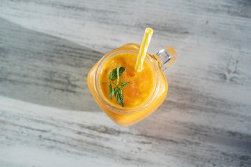 Fresh organic yellow smoothie in glass mug on white wooden table, close up. Refreshing summer fruit drink. The concept of healthy eating. Sea buckthorn smoothie