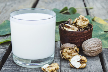 Vegan nut milk in a glass near walnuts on an old wooden table. Vegan milk from walnuts. Eco food.