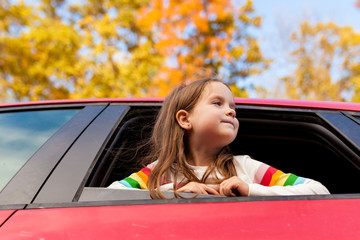 Outdoor recreation and awesome adventures with kids in fall. Young child girl looking out of a car window during a family trip to nature on a warm autumn day. Exploring nature, travel, family vacation