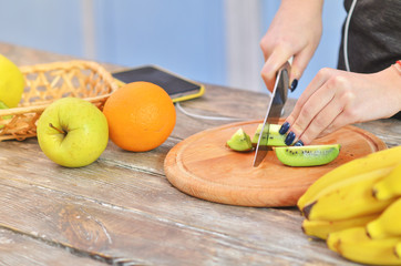 Hands of young girl in sportswear cutting kiwi on chopping board.