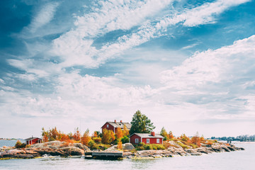 Suomi Or Finland. Beautiful Red Finnish Wooden Log Cabin House On Rocky Island Coast In Summer Sunny Evening. Lake Or River Landscape. Tiny Rocky Island Near Helsinki, Finland - obrazy, fototapety, plakaty