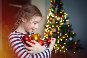 Fototapeta na wymiar child decorates Christmas tree balls. portrait of a girl on the background of Christmas lights