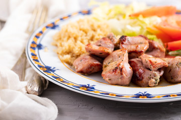 fried meat with quinoa and fresh salad on plate on ceramic background