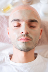 Obraz premium Man with green clay mask on his face. Male grooming, taking self care concept: applying natural treatment to skin