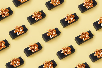 A group black gift box with golden bow on top . Minimal composition for the holiday design goals. Seamless concept pattern. Festive pastel background in trendy color