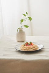 Food, spaghetti bolognese sauce in white dish and a vase of plants on a white prepared table
