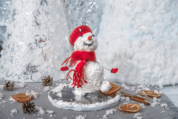 Figure walking on human snowman in red accessories against the background of New Year and Christmas decorations