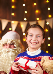 Child girl accepting gifts from Santa near decorated xmas tree with lights, they talking and smiling - Merry Christmas and Happy Holidays!