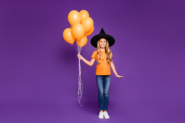 Full size photo of little witch lady halloween party holding many air balloons came to children theme party wear orange t-shirt wizard hat isolated purple color background