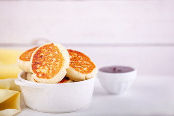 Syrniki - russian ukrainian traditional dessert cottage cheese pancakes in white cup with berry jam with copy space.