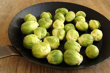 fresh brussels sprouts in an iron pan on a wooden board