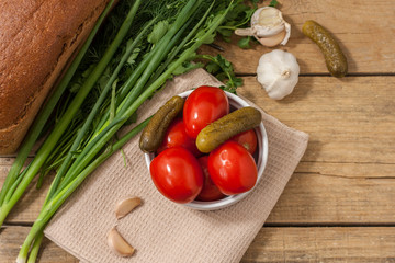 Fermented food on a white plate on an old wooden table. Pickled tomatoes and cucumbers. Salt for the winter. Traditional snack for alcohol.
