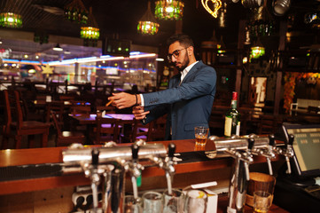 Handsome well-dressed arabian man with glass of whiskey and cigar posed at pub.