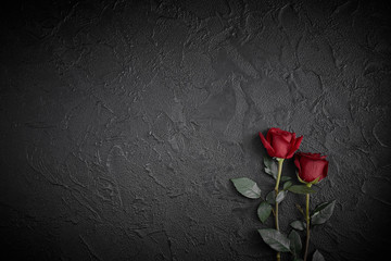 Red roses are placed on a black textured background. A sign of condolence, sympathy loss. Space for your text