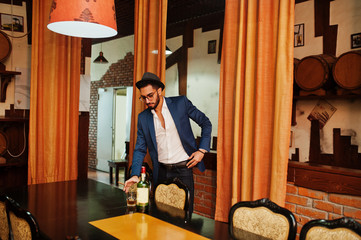 Handsome well-dressed arabian man with glass of whiskey and cigar posed at pub.