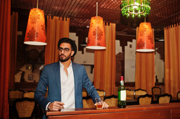 Handsome well-dressed arabian man with glass of whiskey and cigar posed at pub.