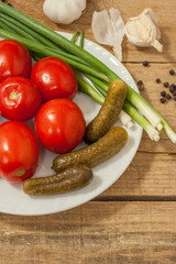 Fermented food on a white plate on an old wooden table. Pickled tomatoes and cucumbers. Salt for the winter. Traditional snack for alcohol.