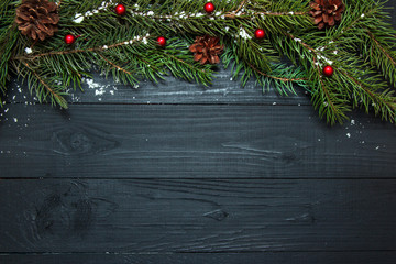 Green branches of a Christmas tree on a black wooden background. Copy space, flat lay.