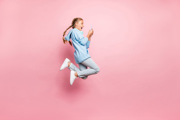 Fototapeta na wymiar Full length body size photo of excited crazy ecstatic schoolchild browsing through phone jumping wearing blue sweatshirt sweater sportive wear jeans denim isolated over pink pastel color background