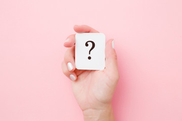Card of question mark in young woman hand on pastel pink background. Concept of plans, thoughts or other good ideas for making decision. Closeup. - obrazy, fototapety, plakaty