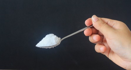 Hand holding spoon of sugar on black background.
