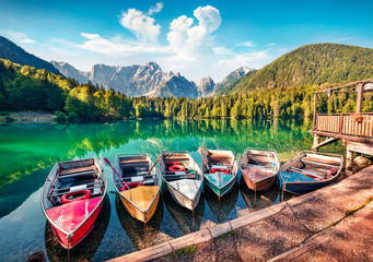 Six pleasure boats on Fusine lake. Bright morning scene of Julian Alps with Mangart peak on...