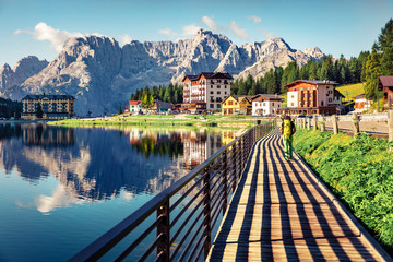 Naklejka premium Tourist walking on the pier on Misurina lake. Sunny morning scene of Misurina resort, National Park Tre Cime di Lavaredo, Location Auronzo, Dolomiti Alps, South Tyrol, Italy, Europe. Retro filtered.