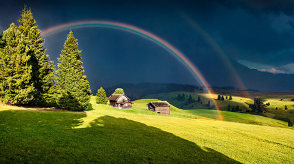 Impressive evening scene of Compaccio village with huge rainbow on background,  Alpe di Siusi...