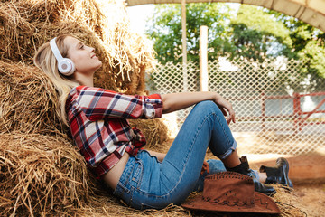 Smiling young blonde cowgirl sitting on a haystack at the barn