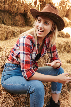 Beautiful cheerful young blonde cowgirl sitting at the barn