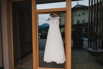 Modern bridal fashion. White wedding dress hanging in the hotel room.