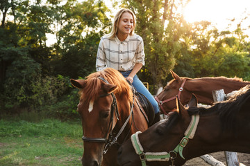 Smiling attractive young blonde girl riding a horse