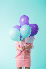 girl in pink outfit holding balloons in front of face isolated on turquoise