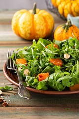 Delicious salad with arugula, baked pumpkin, hazelnut and sesame seeds on brown plate. Paleo diet food concept.