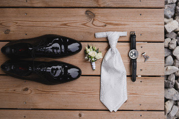 Wedding fashion for men. Top view of boutonniere, shoes, watch, cufflinks and tie on wooden background.