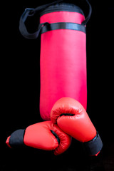 Red boxing gloves and a boxing bag for punches on a black background