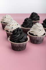 delicious Halloween cupcakes with white and black cream on pink surface isolated on white